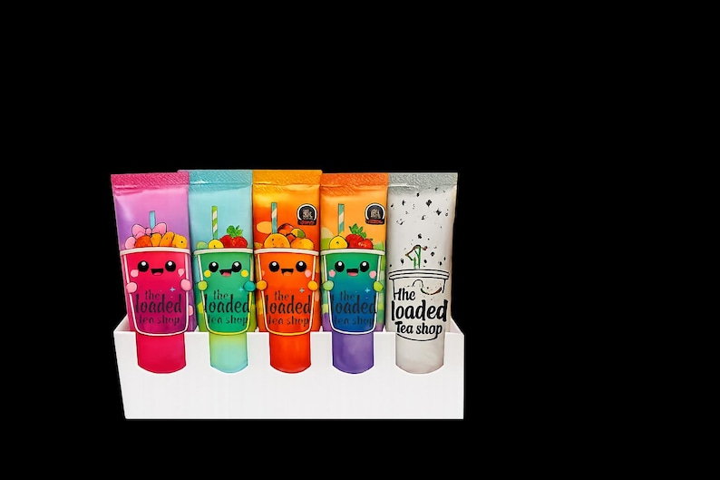 May include: A display of six colorful, squeezable drink pouches in a white holder. Each pouch features a cartoon cup design with fruit and the text "The Loaded Tea Shop". The pouches are pink, blue, orange, green, purple, and white.