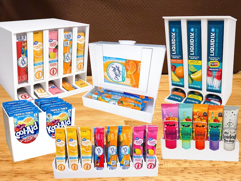 May include: Assortment of drink mix packets and tubes in white display cases. Brands include Crystal Light, Kool-Aid, and Liquid I.V. Flavors include citrus, tropical punch, and various fruit blends. The Loaded Tea Shop tubes are also visible.