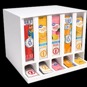 May include: A white wooden drink mix organizer with six vertical slots holding various flavored drink mix packets. The bottom row has matching packets. The packets are labeled with fruit images and the words "Sugar Free".