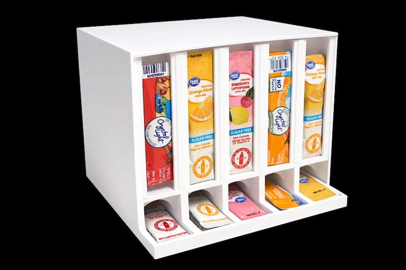 May include: A white wooden drink mix organizer with six vertical slots holding various flavored drink mix packets. The bottom row has matching packets. The packets are labeled with fruit images and the words "Sugar Free".