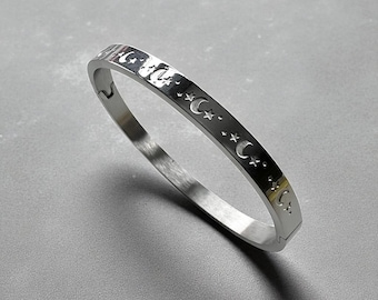 Può includere: Un bracciale rigido color argento con un motivo ripetuto di lune crescenti e stelle. Il bracciale ha un design semplice ed elegante. È realizzato in un materiale metallico lucido. Circonferenza di circa 18 cm.
