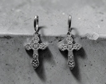 Può includere: Un paio di orecchini a cerchio color argento con pendenti a croce decorati. Ogni croce presenta intricati dettagli in rilievo e una finitura metallica lucida. Gli orecchini sono dotati di un meccanismo a cerniera per il lobo dell'orecchio.