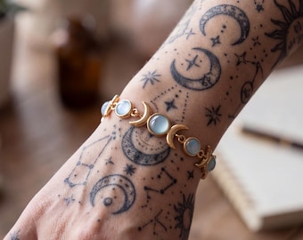Può includere: Un bracciale color oro caratterizzato da una serie di ciondoli a forma di mezzaluna alternati a pietre cabochon rotonde di colore azzurro pallido. Il bracciale è progettato con una struttura a catena, che mostra un motivo celeste che collega ogni elemento.