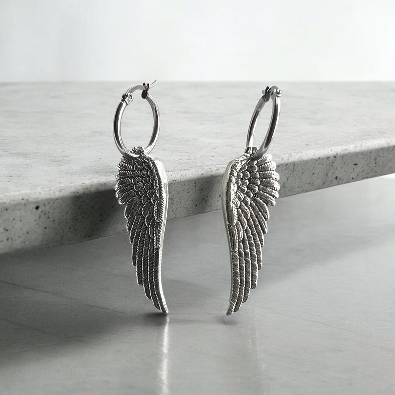 May include: A pair of silver hoop earrings with angel wing charms. The wings are detailed and have a textured finish.