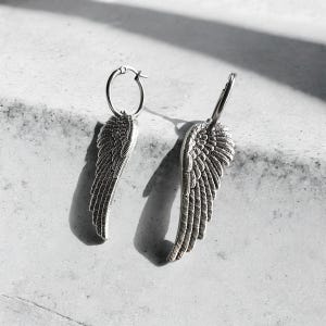 May include: A pair of silver hoop earrings with angel wing charms. The wings are detailed and have a textured finish.