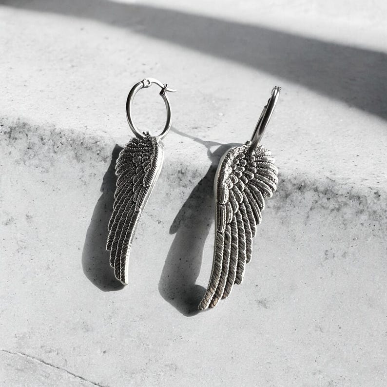 May include: A pair of silver hoop earrings with angel wing charms. The wings are detailed and have a textured finish.