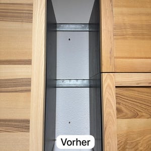 Puede incluir: Vista de cerca del interior de un mueble de cocina. Las puertas del armario son de madera clara con vetas visibles. La palabra "Vorher" se muestra en un óvalo blanco. Se ven rieles metálicos dentro del armario.