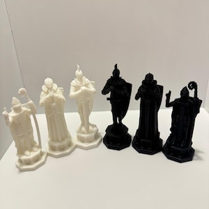May include: A chess set featuring medieval-themed pieces. The pieces are in black and white, with detailed knight, bishop, and king designs. The chess pieces are arranged on a white surface.
