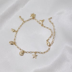 May include: Gold anklet with a variety of charms, including a seashell, starfish, and a ship's wheel. The anklet is made of a delicate chain and has a lobster clasp closure.