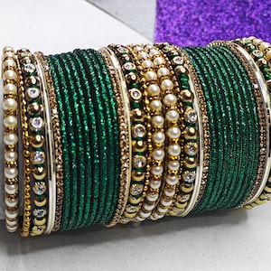Può includere: Un set di braccialetti verdi e dorati con dettagli di perle bianche e strass. I braccialetti sono impilati uno sull'altro e sono un accessorio popolare per i matrimoni indiani e altre occasioni speciali.