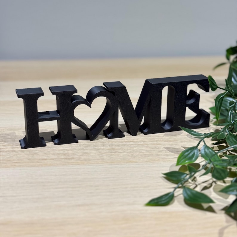 Side angle view of 3D printed white HOME sign on a wooden surface showing depth and freestanding design