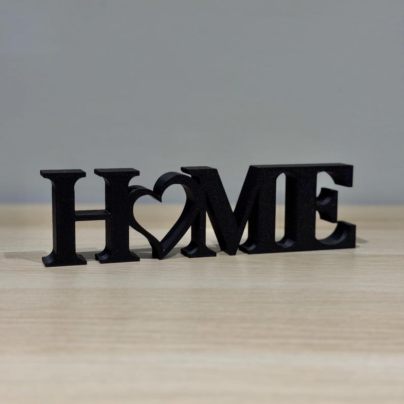 3D printed HOME sign with heart detail in black on a dark surface showing bold contrast and clean lettering