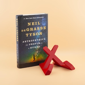 May include: A red book stand with a book titled "Astrophysics for People in a Hurry" by Neil deGrasse Tyson. The book is a #1 New York Times Bestseller.