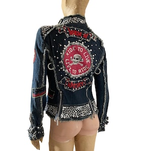 May include: A dark blue denim jacket with a red and white embroidered patch that says "Live to Ride, Ride to Live" with a skull and crossbones. The jacket is covered in rhinestones and has a frayed hem.