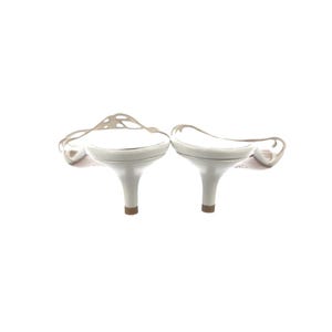 May include: A pair of white heeled sandals. The sandals feature a delicate, open strap design and a small heel. The shoes are set against a white background.
