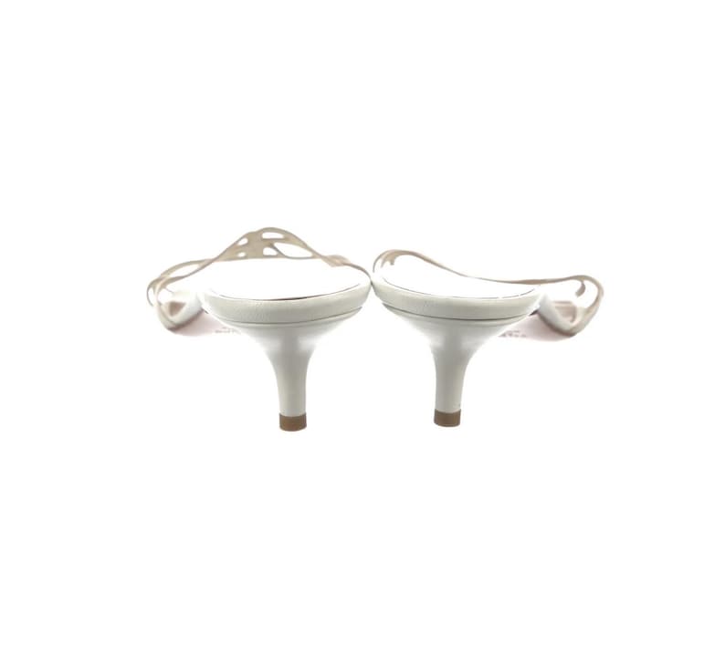May include: A pair of white heeled sandals. The sandals feature a delicate, open strap design and a small heel. The shoes are set against a white background.