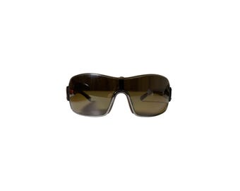 Puede incluir: Gafas de sol marrones oscuras con lentes tintadas. Las gafas tienen un diseño envolvente, que ofrece un aspecto elegante y moderno. Las lentes parecen tener un tinte degradado, que pasa de un tono más oscuro en la parte superior a un tono más claro en la parte inferior.
