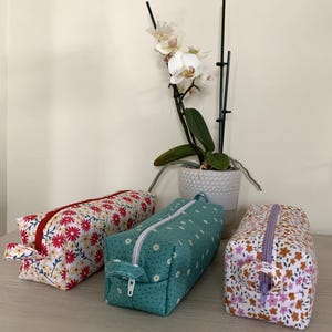 May include: Three zippered pouches with floral patterns. The pouches are made of fabric and have a zipper closure. The pouches are in different colours and patterns. The pouches are on a table with a plant in the background.