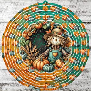 Op de afbeelding: Een ronde herfstdecoratie met een vogelverschrikker in een tuinbroek, omringd door pompoenen en bladeren. Het ontwerp bevat de tekst "Fall Y'all" tegen een verloop van oranje, groen en wit. Met een ophanglus.