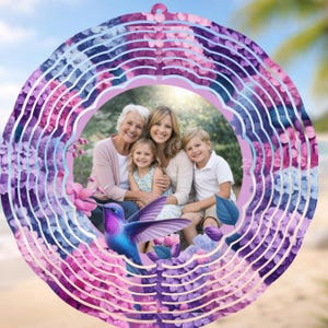 May include: A decorative wind spinner featuring a family portrait surrounded by a floral design. The spinner has a layered, circular design with shades of purple, pink, and blue. A hummingbird is featured at the bottom of the image.