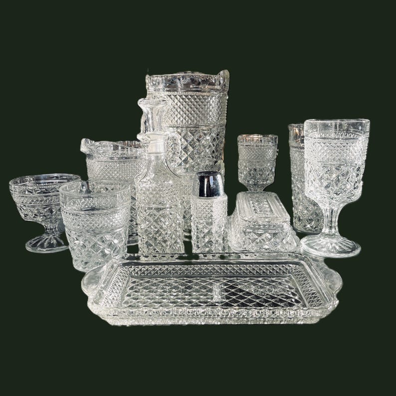 May include: A collection of clear, diamond-patterned glassware, including a pitcher, glasses, a tray, and a sugar bowl. The set is arranged on a dark green background, showcasing the intricate details of each piece. The glassware appears to be vintage.