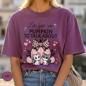 May include: Berry-coloured t-shirt with the text "Lets give 'em PUMPKIN TO TALK ABOUT". The graphic features a pink pumpkin with a bow, two cats, and hearts. A fall-themed design.