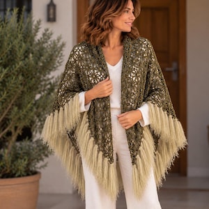 Può includere: Uno scialle all'uncinetto verde oliva caratterizzato da un motivo floreale ripetuto e lunghe frange beige chiaro lungo i bordi. Il capo è drappeggiato sulle spalle, mostrando un intricato design traforato dall'aspetto strutturato e annodato.