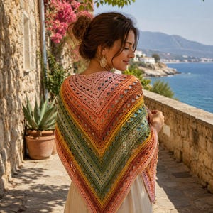 Puede incluir: Un chal triangular de ganchillo con un degradado vibrante de colores que incluye rosa suave, naranja cálido, amarillo dorado y verde oliva intenso. El chal presenta un intrincado patrón de calados con un borde texturizado y puntas.