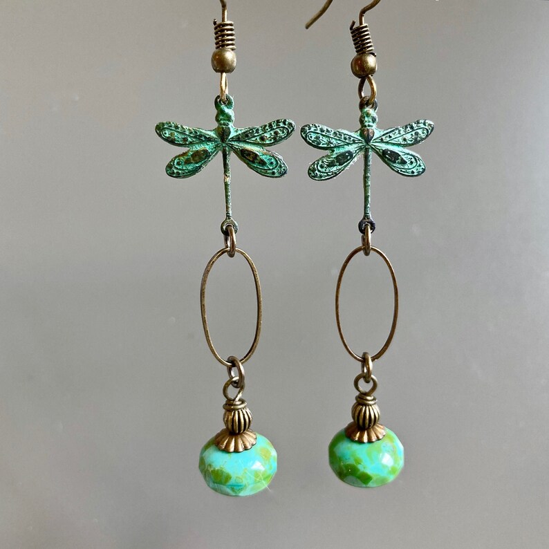 May include: A pair of dangle earrings featuring a green dragonfly charm and a turquoise bead. The earrings are made of brass and have a vintage look.