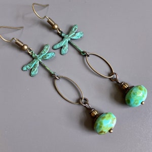 May include: A pair of dangle earrings with a turquoise dragonfly charm and a turquoise gemstone bead. The earrings are made of brass and have a vintage look.