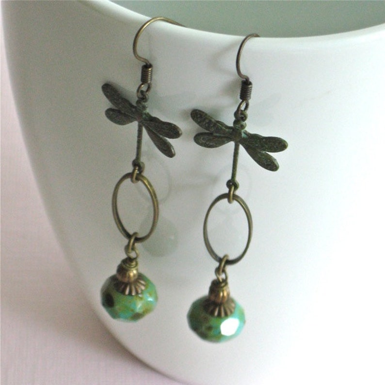 May include: A pair of dangle earrings with a dragonfly charm and a turquoise bead. The dragonfly is made of metal and has a bronze finish. The bead is round and has a faceted surface.
