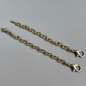 Puede incluir: Dos cadenas de metal dorado con cierres de langosta. Las cadenas están unidas en un extremo y tienen una pieza de extremo decorativa en el otro.