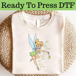 May include: A white t-shirt with a cartoon image of Tinkerbell, the fairy from Peter Pan, with the text "All You Need Is Faith, Trust, and Pixie Dust".
