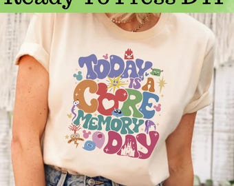 Op de afbeelding: Crèmekleurig T-shirt met een kleurrijke afbeelding met de tekst "Today is a Core Memory Day". Het ontwerp bevat verschillende cartoon-elementen in blauw, oranje, groen en roze. De tekst "Ready To Press DTF" staat bovenaan.