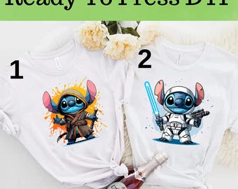 May include: Two white t-shirts with a blue Stitch character wearing different costumes. The first shirt has Stitch dressed as a Jedi, and the second shirt has Stitch dressed as a Stormtrooper. The shirts are numbered 1 and 2.