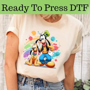 May include: A white t-shirt with a colorful graphic print of Mickey Mouse and Pluto. The graphic features a rainbow and colorful paint splatters.