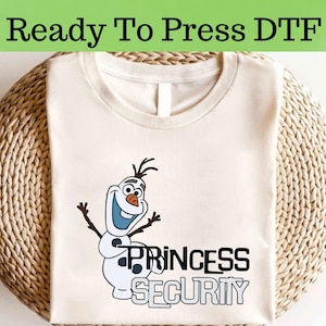 以下が含まれることがあります： ベージュのTシャツに、アナと雪の女王のオラフの漫画の画像がプリントされています。オラフの下には「Princess Security」という文字がプリントされています。