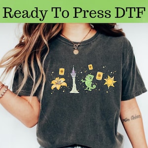 May include: A dark gray t-shirt with a graphic print of a tower, a chameleon, a flower, and a sun. The text "Ready To Press DTF" is at the top of the image.