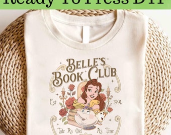 May include: Cream-colored t-shirt with the text "Ready To Press DTF" at the top. The shirt features a graphic for "Belle's Book Club" with Belle, roses, and the text "Tale As Old As Time" and "Est 1991."