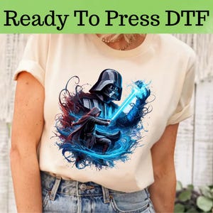 May include: A white t-shirt with a graphic print of Darth Vader and a character from Star Wars. The graphic is in a blue and red color scheme with a splash of paint effect.