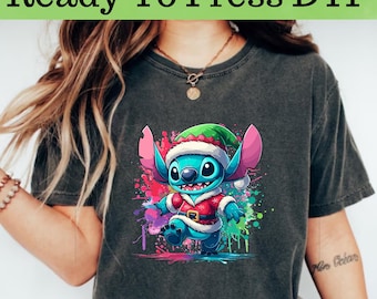 May include: A dark gray t-shirt with a colorful graphic of a blue Stitch character wearing a Santa hat and red and white suit. The character is standing on a colorful splatter background.