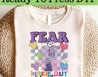 Op de afbeelding: Crèmekleurig T-shirt met het woord "FEAR" in paarse bubbelletters, een stripfiguur en ballonnen. Het shirt bevat ook de tekst "INSIDE OUT" en de naam "Christiana". De woorden "Ready To Press DTF" staan bovenaan.