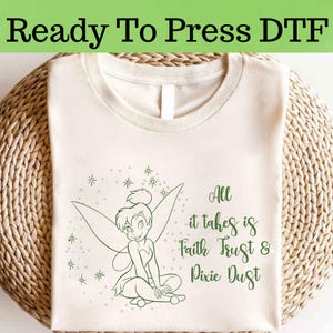 May include: A white t-shirt with a green outline of Tinkerbell sitting with her wings spread. The text "All it takes is Faith Trust & Pixie Dust" is written below her.