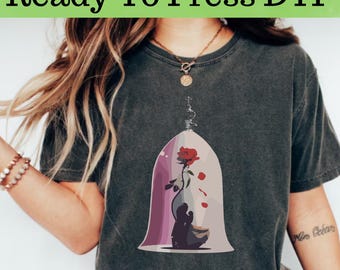 Könnte beinhalten: Dunkelgraues T-Shirt mit einer Grafik einer roten Rose in einer Glaskuppel und einer Silhouette. Der Text "Ready To Press DTF" steht oben in Grün.