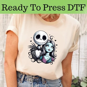 Peut inclure: Un t-shirt blanc avec un imprim&eacute; graphique de Jack Skellington et Sally du film L'&Eacute;trange No&euml;l de monsieur Jack. Le graphique est en noir, blanc, bleu et violet.
