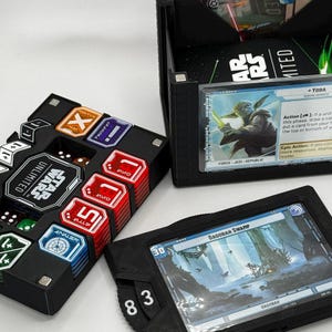 Könnte beinhalten: Schwarze Star Wars Unlimited Kartenspiel-Organizer. Ein Organizer enthält Karten mit einem Yoda-Bild, ein anderer Karten mit einem Dagobah Swamp-Bild. Ein dritter enthält Würfel und Token.