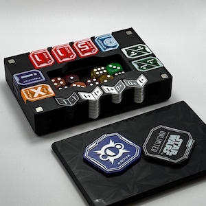 May include: A black game organizer with various game pieces, including dice and tokens. The organizer has compartments for different game components. Some tokens have the text "STAR WARS UNLIMITED". The dice are various colors, and the tokens are red, orange, and blue.