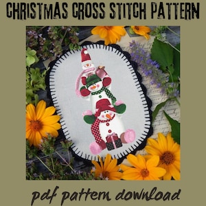 Könnte beinhalten: Ein ovales Kreuzstichmuster mit drei übereinander gestapelten Schneemännern. Die Schneemänner tragen Hüte, Schals und Fäustlinge in Rot, Grün und Rosa. Der Text "CHRISTMAS CROSS STITCH PATTERN" und "pdf pattern download" sind vorhanden.