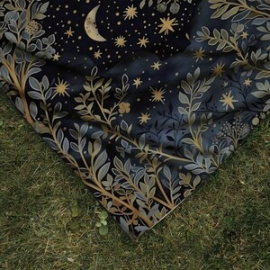 and fabric drape, botanical sage green foliage with crescent moon and golden stars on dark navy blue background, outdoor nature photography demonstrating cozy witchy boho blanket quality and flexibility