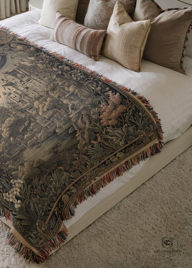 May include: A woven tapestry throw blanket featuring a detailed dark-toned landscape scene with architectural structures, lush foliage, and floral elements. The blanket has a decorative fringe border with multi-colored threads along the edges.
